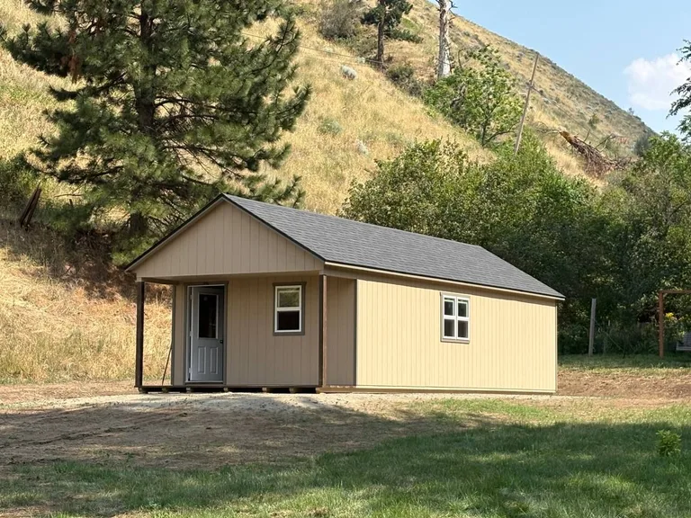 Tan cabin with covered porch and gray shingle roof on a hillside property