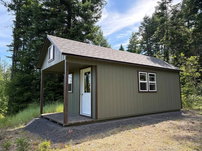 Olive green cabin with 4-foot porch, loft window, and double side windows in the woods