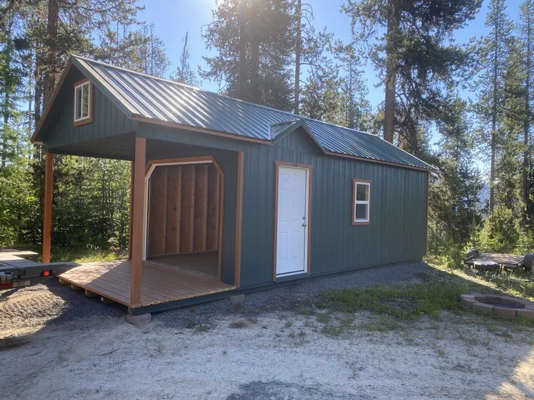 Forest green cabin with green metal roof and extended porch deck among tall pines