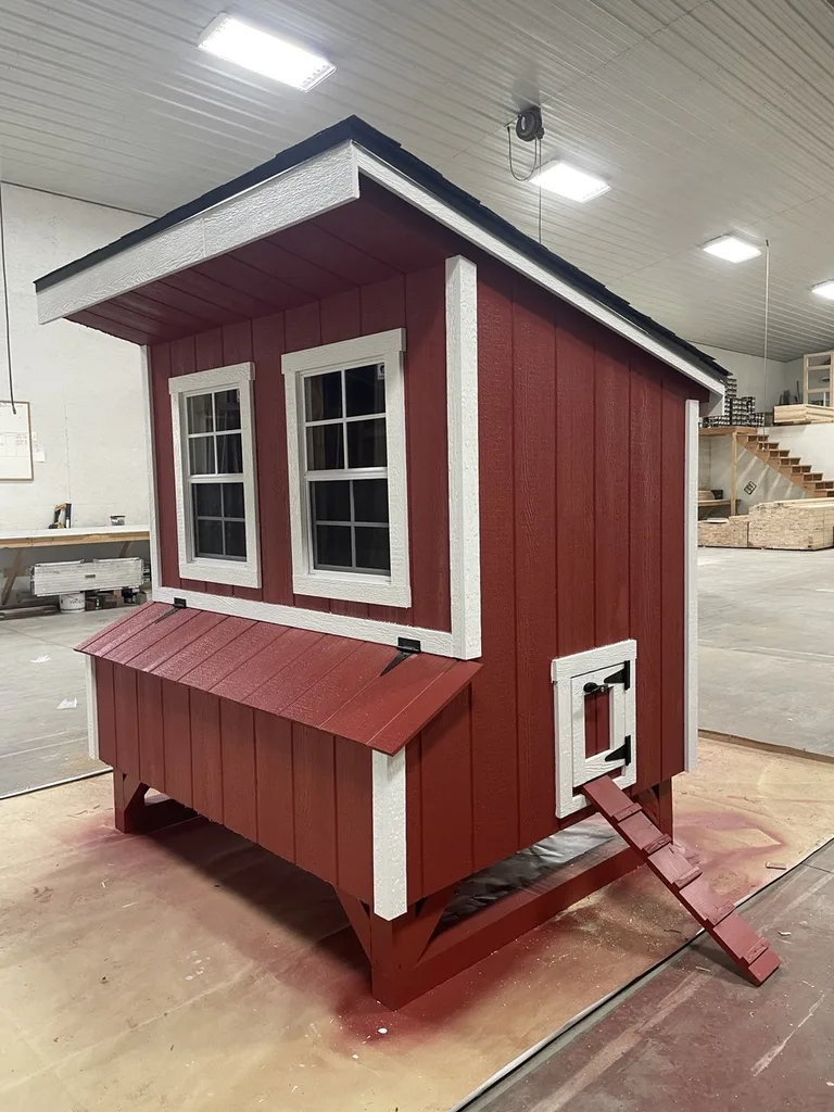 Red chicken coop with white trim, two windows, chicken door, and ramp in the workshop