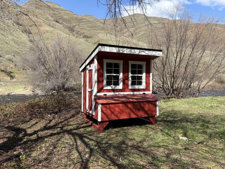 Red chicken coop with white trim beside the river