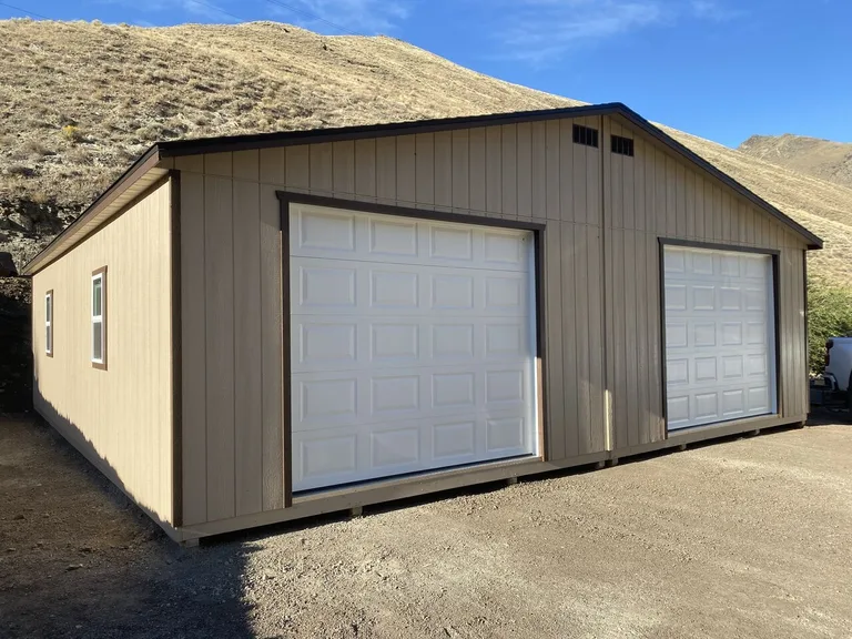 Tan double-wide garage with two white overhead doors against a golden hillside
