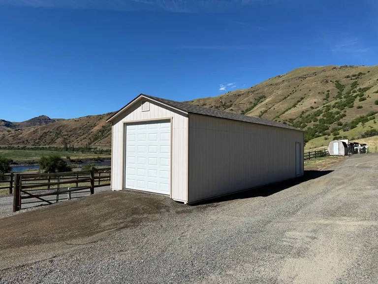 Cream garage with white overhead door along a gravel road in the foothills