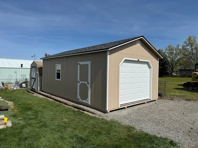 Tan garage with white overhead door and side entry door in a backyard