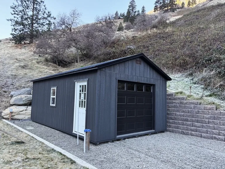 Charcoal garage with black overhead door, white entry door, and windows against a hillside
