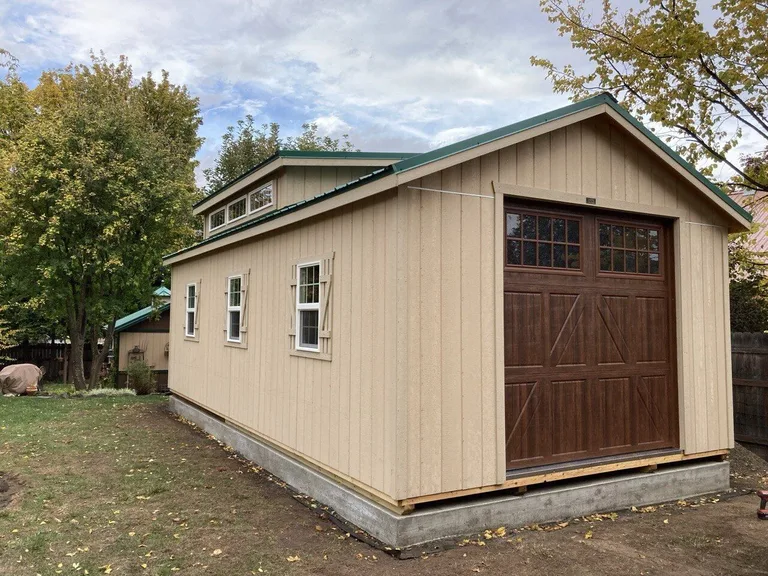 Tan garage with wooden carriage-style overhead door, dormer windows, and green roof