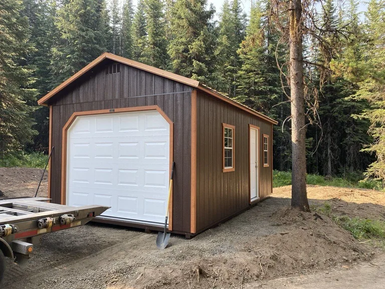 Brown garage with white overhead door and tan trim among tall pines