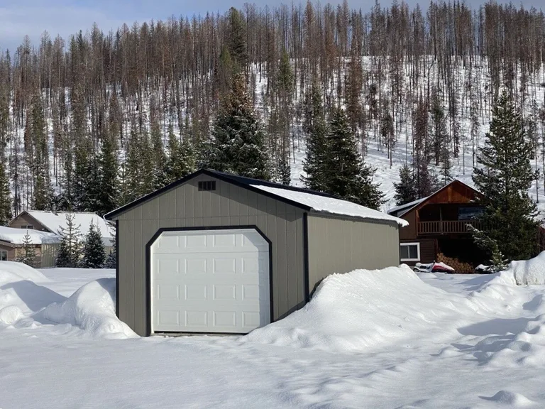 Gray garage with white overhead door on a snowy mountain property