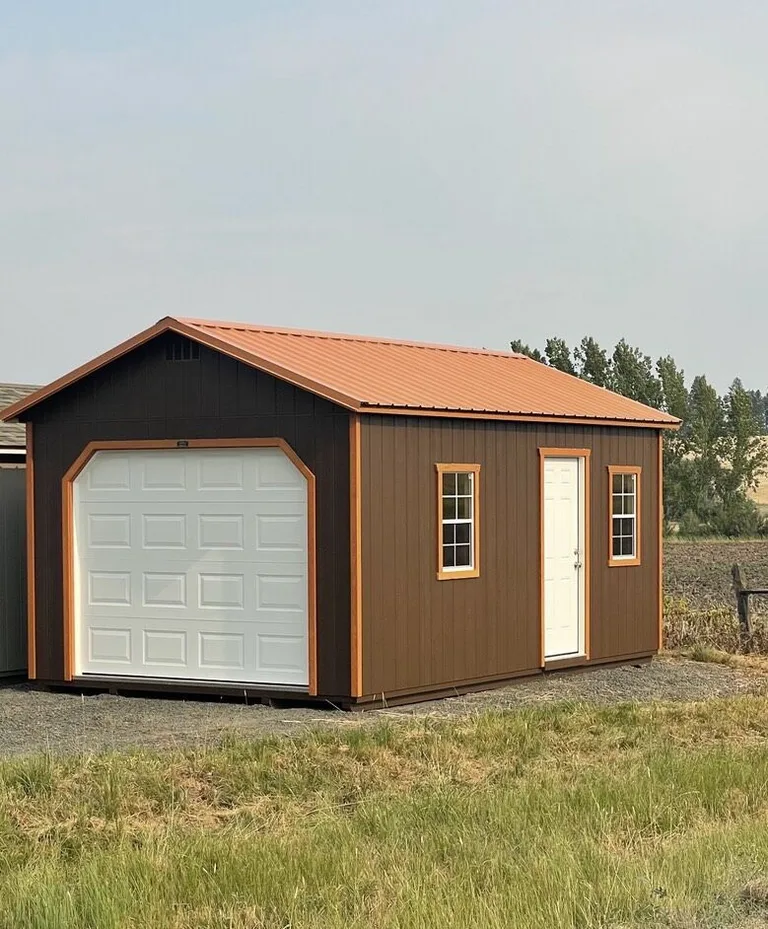 Brown garage with orange trim, entry door, and windows in an open field