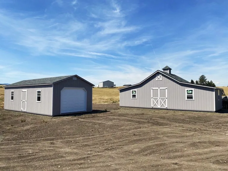 Gray garage with white overhead door on a display lot next to a carriage barn