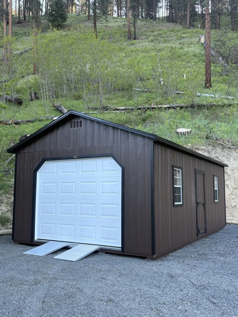 Dark brown garage with white overhead door and side windows on a gravel drive