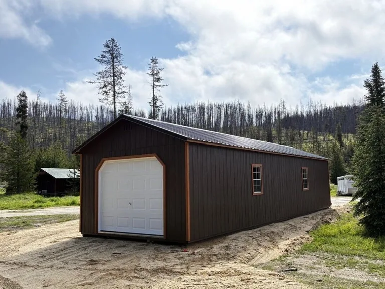 Long dark brown garage with orange trim on a rural mountain property
