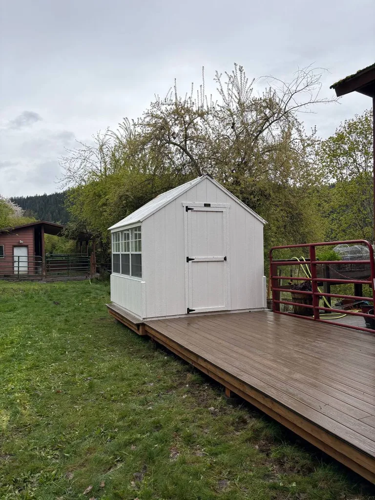 White greenhouse with side windows installed beside a backyard deck