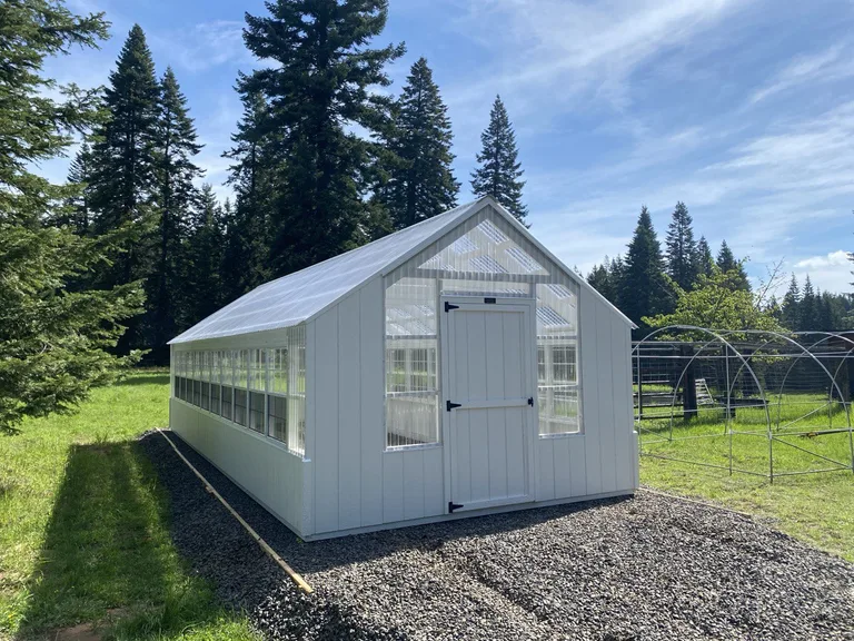 Long white greenhouse with poly roof and endwall on a gravel pad