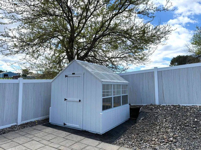 White greenhouse with poly roof in a fenced backyard garden