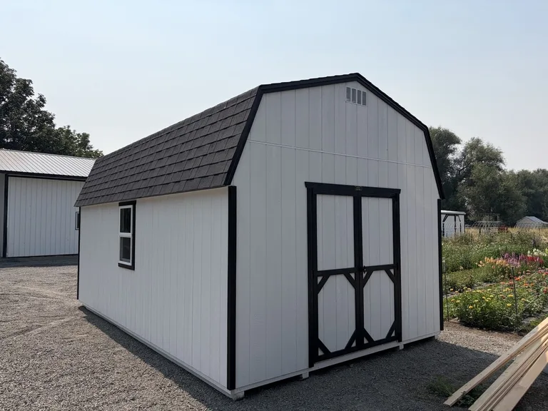 White high barn style shed with black trim, double doors, and gambrel roof on a display lot