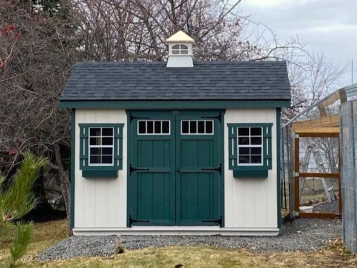 White carriage shed with green double doors, window shutters, and a cupola