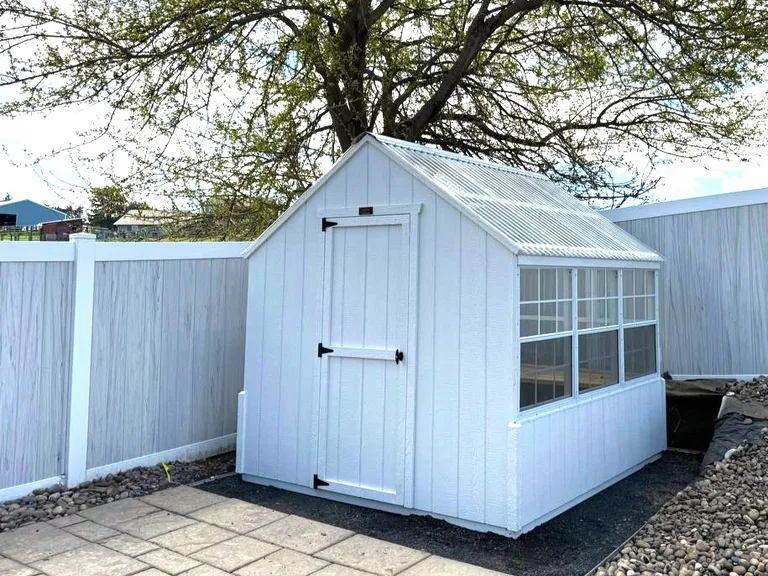 White backyard greenhouse with clear roofing and a row of side windows