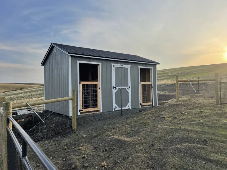 Gray horse barn with white trim, two open stall doors, and a center walk door on a pasture