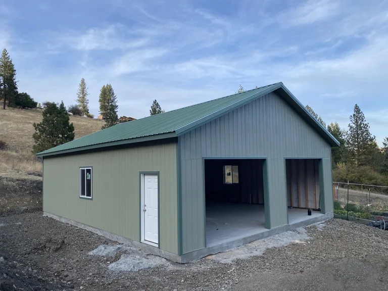 Green metal-sided garage with matching metal roof on a hillside property