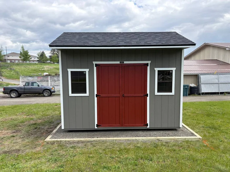 Gray Quaker style shed with red double doors and two shuttered windows