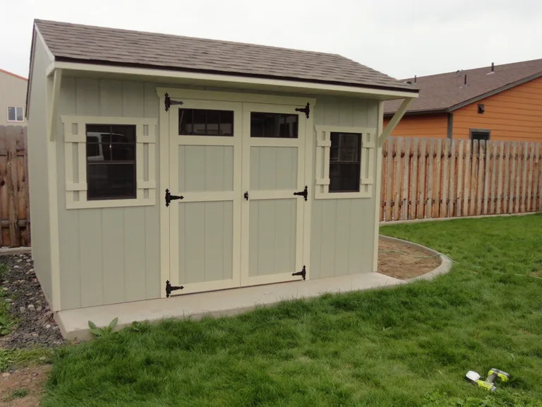Sage green Quaker style shed with double doors, transom windows, and front overhang