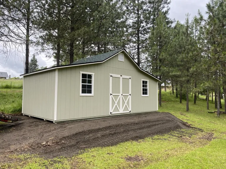 Sage green Rancher barn with white trim double doors set among tall pines