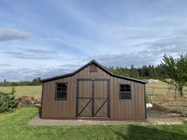 Dark brown Rancher barn with black trim double doors and two windows on a rural property