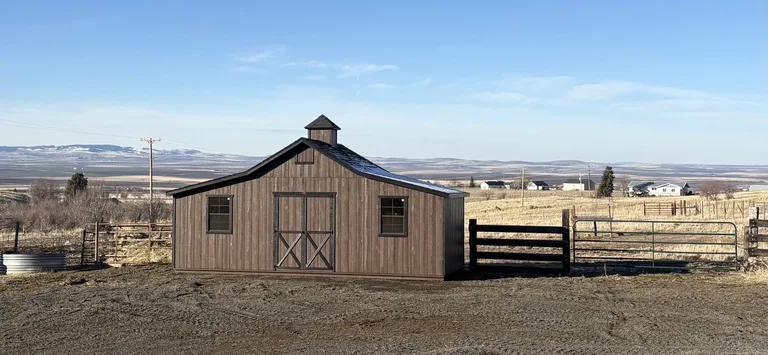 Rustic wood-tone Rancher barn with cupola beside a corral fence with valley views