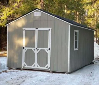 Gray utility style shed with white trim doors in the snow