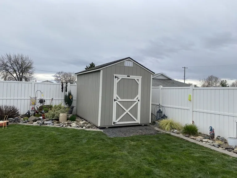 Gray utility style shed with white trim door in a landscaped backyard