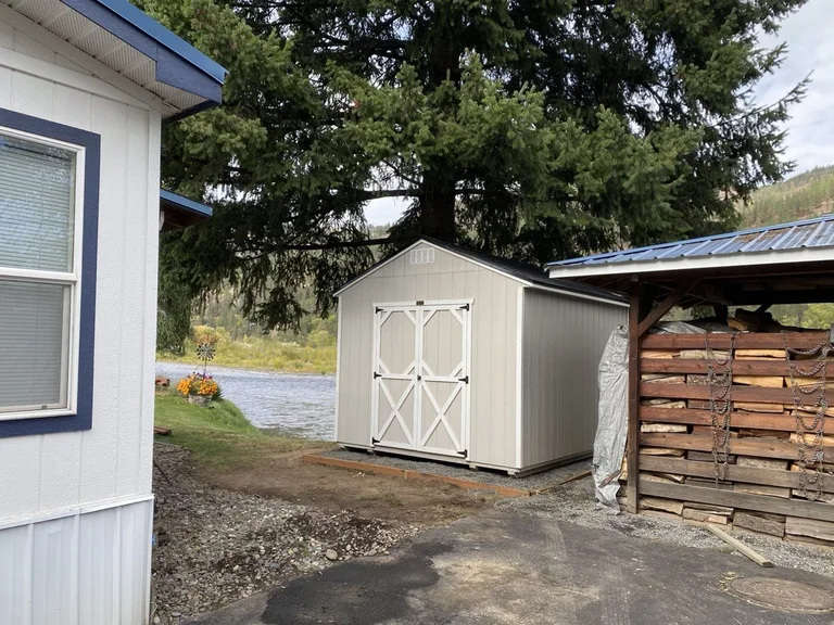 Tan utility style shed with double doors beside the river